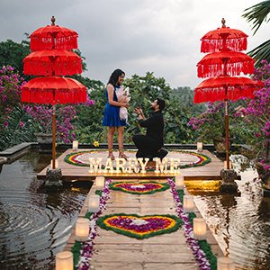 Man proposing on a candlelit wooden deck with Marry Me letters between two red umbrellas